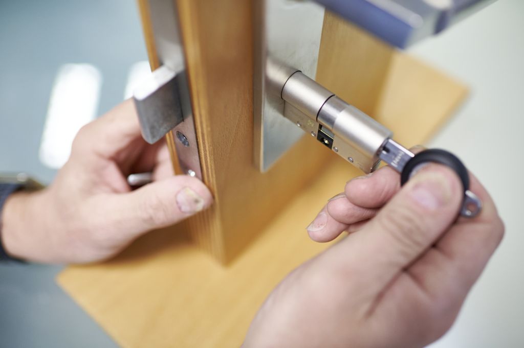 Nahaufnahme von Händen, die ein modernes zylindrisches Türschloss in eine Holztür einbauen. Zur Präzision wird dabei ein Schraubenzieher verwendet.