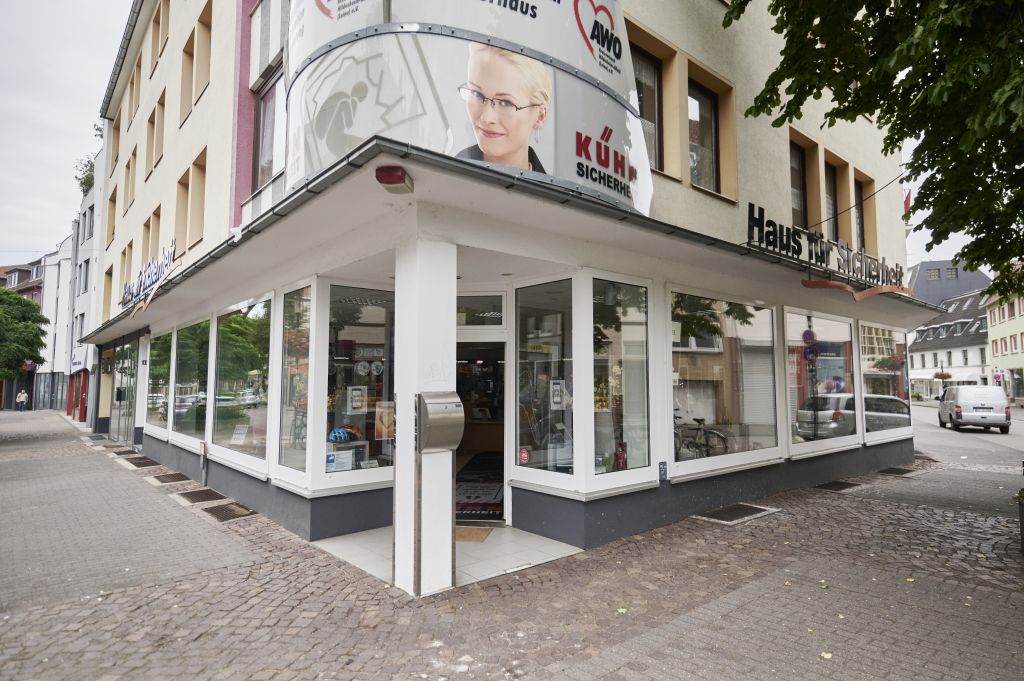 Eckansicht eines modernen Optikergeschäfts mit großen Glasfenstern, auf denen Werbung für Augenpflegeprodukte gezeigt wird, in einem Stadtgebiet.